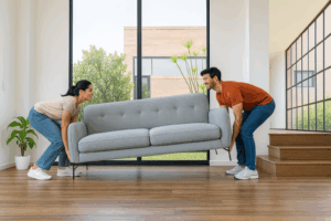 Young first home buyers lifting a sofa inside their new Australian home, symbolising moving in, setting up their space, and starting their homeownership journey.