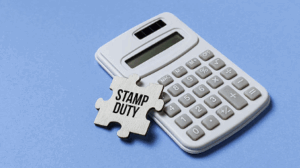 High-resolution image of a stamp duty puzzle piece placed beside a calculator on a blue background, representing stamp duty calculations for property buyers.