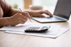 Person using a calculator and laptop to calculate loan repayments and estimate loan affordability