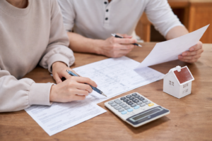 Couple reviewing mortgage application paperwork with calculator and house model on a wooden table