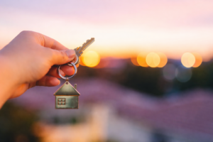 Hand holding house keys with a home-shaped keyring at sunset, representing applying for a home loan through a mortgage broker