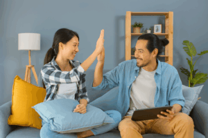 Happy First Home Buyers Celebrating Approval – Mortgage Broker Melbourne Assistance - Find A Better Rate Home Loans Young couple sitting on their couch celebrating a successful home loan approval, representing first home buyers receiving guidance from a Melbourne mortgage broker.