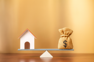 Mini house and money bag balanced on a seesaw, symbolising property price, deposit size, borrowing power and loan-to-value calculation.