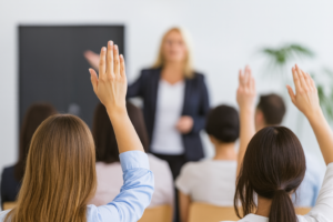 Audience members raising their hands during a home buying information session while a presenter speaks at the front of the room, representing active engagement and property offer education.